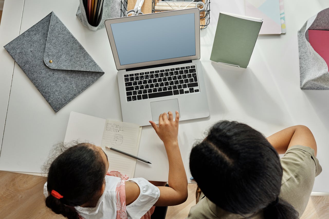 A mother helps her daughter with schoolwork on a laptop at home, promoting education and bonding.