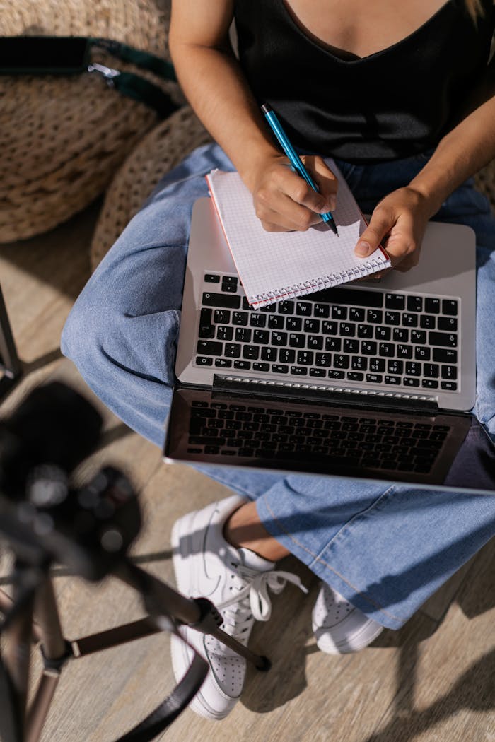 Person taking notes while studying online using a laptop and notebook indoors